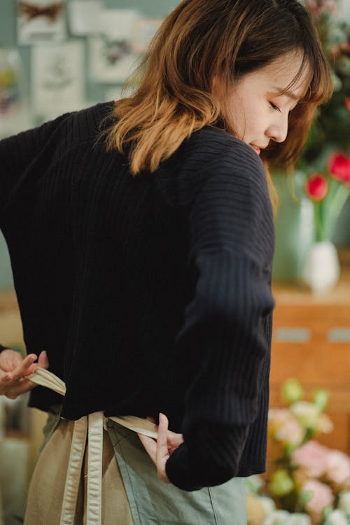 Ethnic florist tying bow on apron while preparing for work