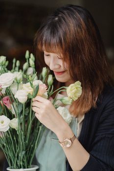 一位亚洲女花店店员手捧一束带着温柔花蕾的新鲜玫瑰，正低头看着