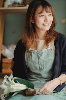 Cheerful florist in apron holding lilies, smiling in workshop.