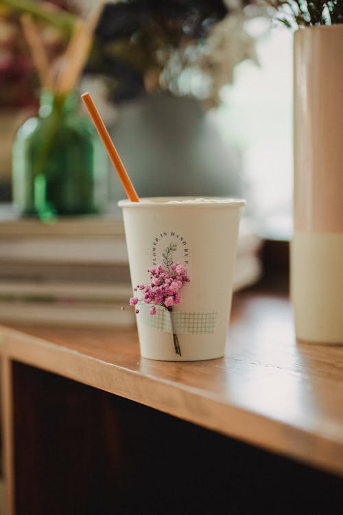 Small white cup decorated with flowers placed on wooden table near vases with flowers