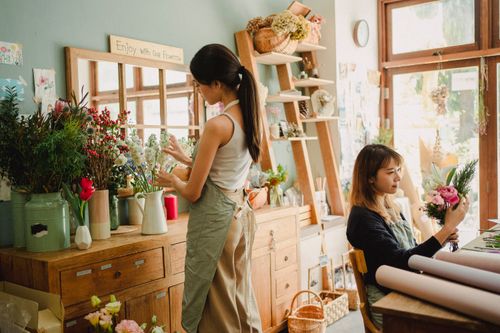 Free Side view of focused Asian female making gentle bunch while working with assistant standing among assorted flowers Stock Photo