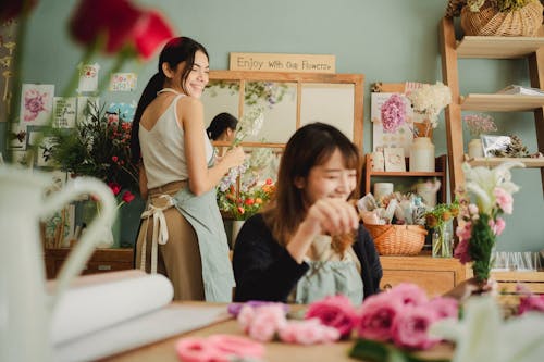 Cheerful multiracial female florists smiling happily while working in floral workshop with various flowers