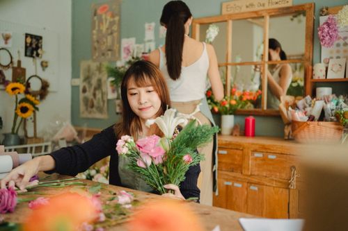 Free Busy Asian florist composing blooming flowers while working in floral shop with colleague Stock Photo