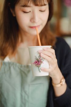 系着围裙的亚洲女性在工作间隙，用装饰着鲜花的杯子享用美味饮料