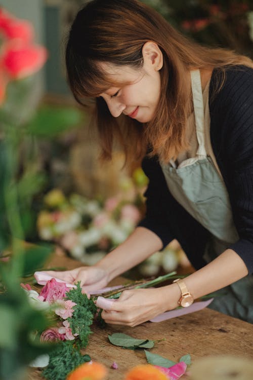 Florist arranging pink flowers at a wooden table in a cozy flower shop setting.