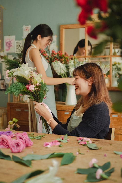 Side view of positive florist tying bouquet of fresh flowers while working with assistant in floral store