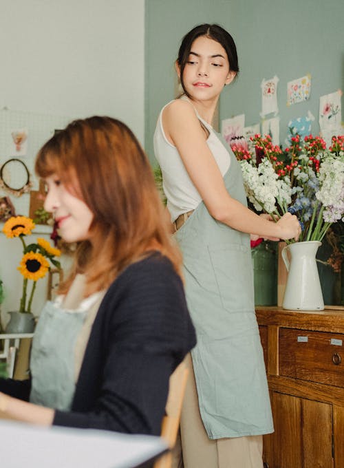 Side view of concentrated young female professional florist arranging flowers while working with colleague at workplace