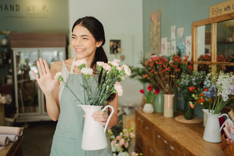 Florist in an apron waving inside her flower shop — photo by Amina Filkins on Pexels