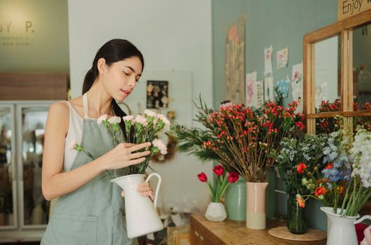 迷人的花店女店员穿着围裙，工作时将鲜花插入花瓶