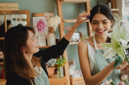 Free Smiling multiracial florists in aprons communicating while working in flower shop with stylish interior Stock Photo