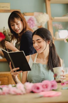 Cheerful female in apron reading notes while communicating with colleague in floral shop