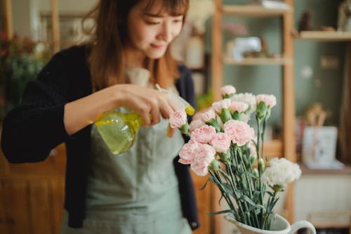 Crop female florist arranging bouquets of flowers and spraying fresh water during work