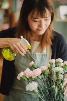 年轻的女花商在花店工作时，系着围裙给鲜花喷洒淡水