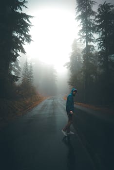 一名全身穿着雨衣的男子在浓雾笼罩的黑暗森林中沿着柏油路行走