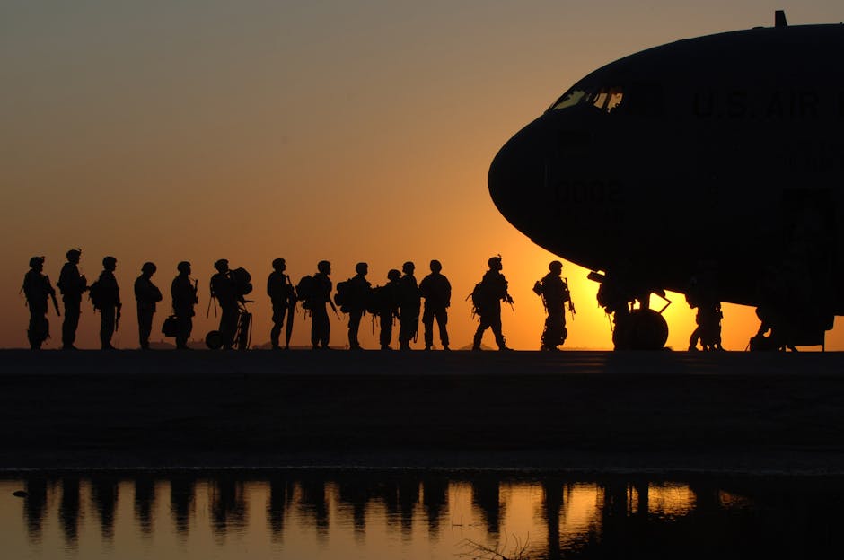 Silhouettes of military service members lining up to board a plane, framed against the backdrop of a sunset. - Enlisting in the U.S. Military