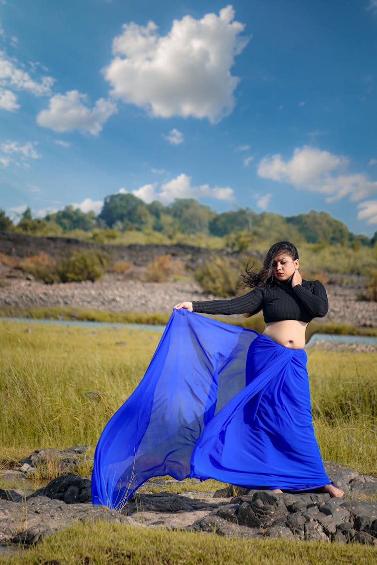 Woman In Black Crop Top And Blue Sarong Standing On Gray Stones