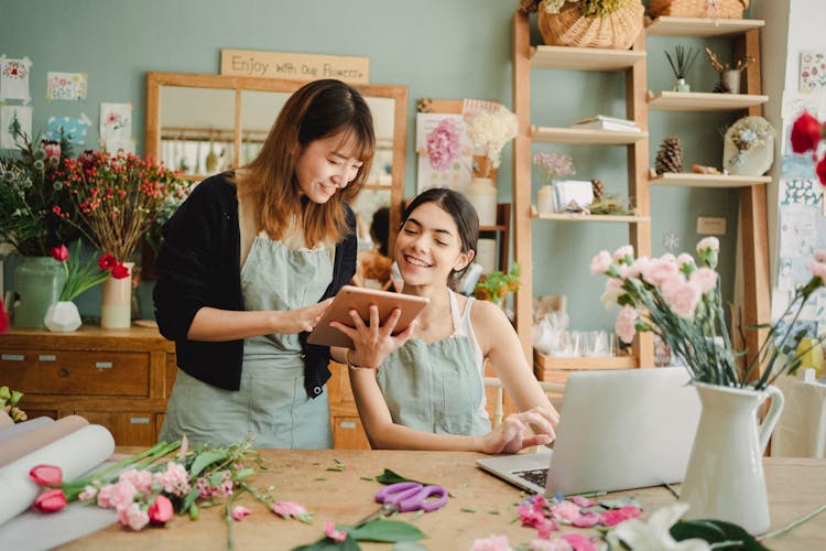 Positive Multiracial Women Working With Tablet In Floral Store