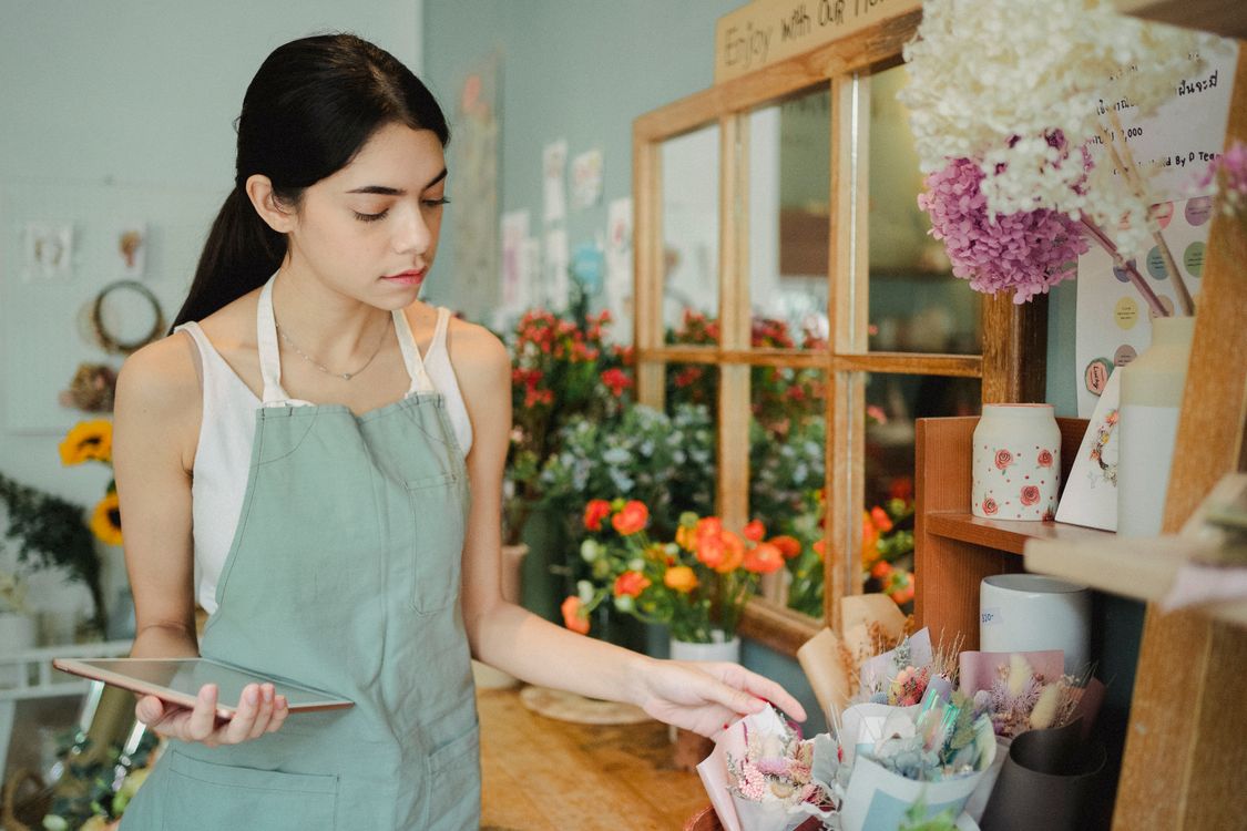 Florist in a green apron checking a tablet beside wrapped bouquets, a reminder to test a new site on a real device