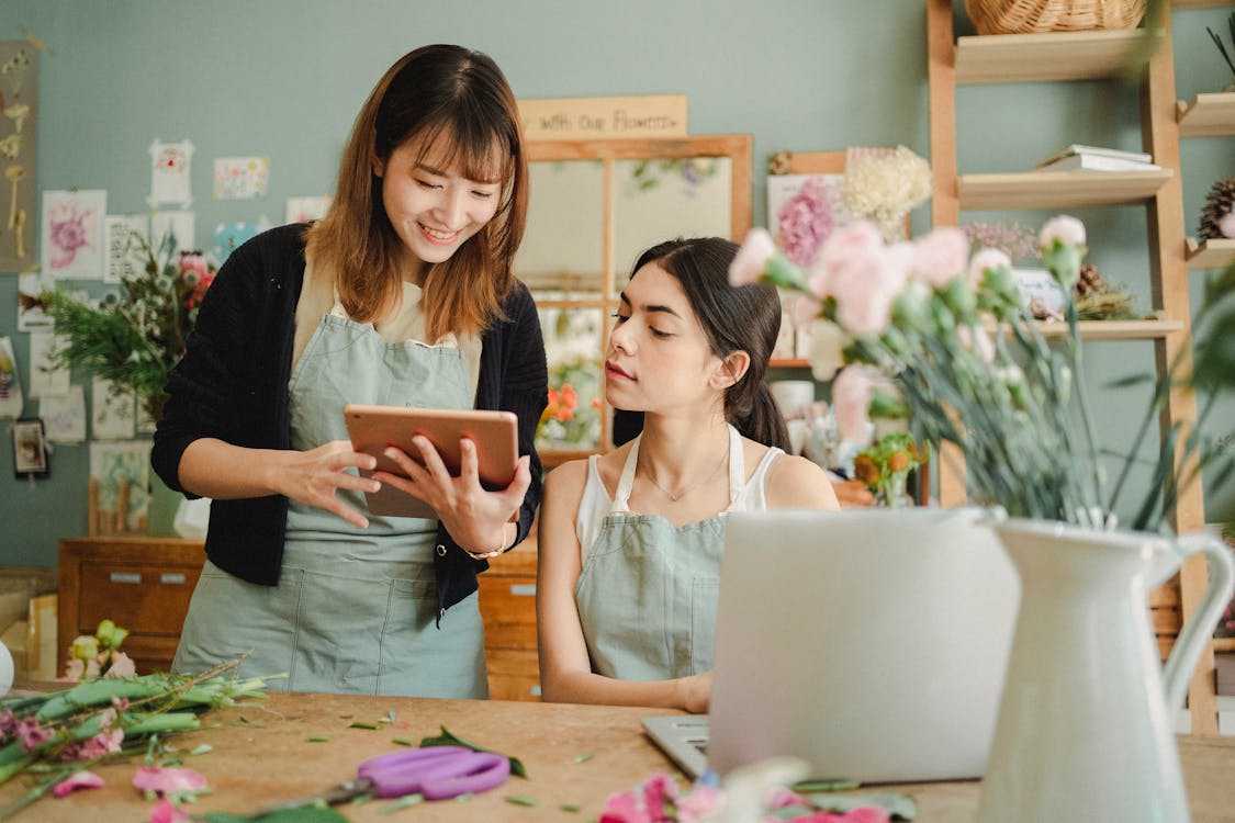 Free Content multiethnic female coworkers at table with flowers surfing tablet while choosing design for bouquet during work in florist shop Stock Photo