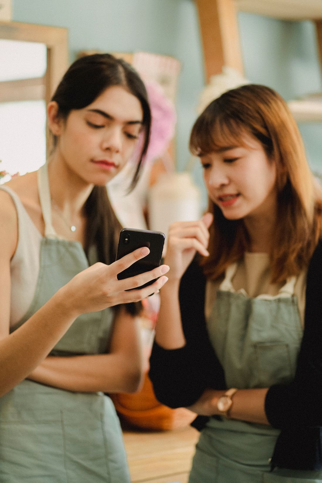 Two shop owners in aprons reacting to something on a phone together. Photo by Amina Filkins on Pexels