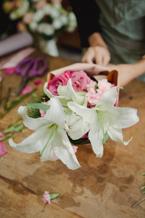 Free Crop unrecognizable female florist arranging bouquet of fresh flowers in paper while working in floral shop Stock Photo