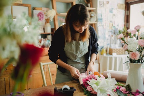 Concentrated Asian female florist arranging flowers in bouquet while working in floral shop