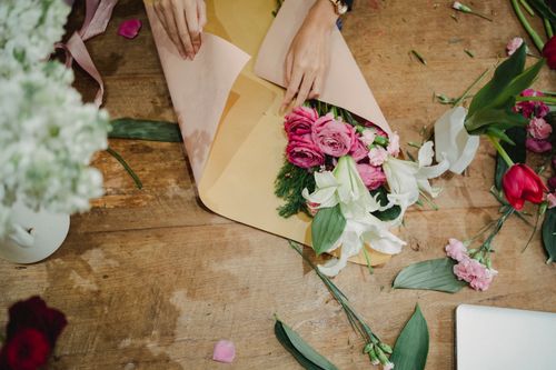 Free Crop faceless female florist holding craft paper and flowers and creating bouquet in floral shop Stock Photo