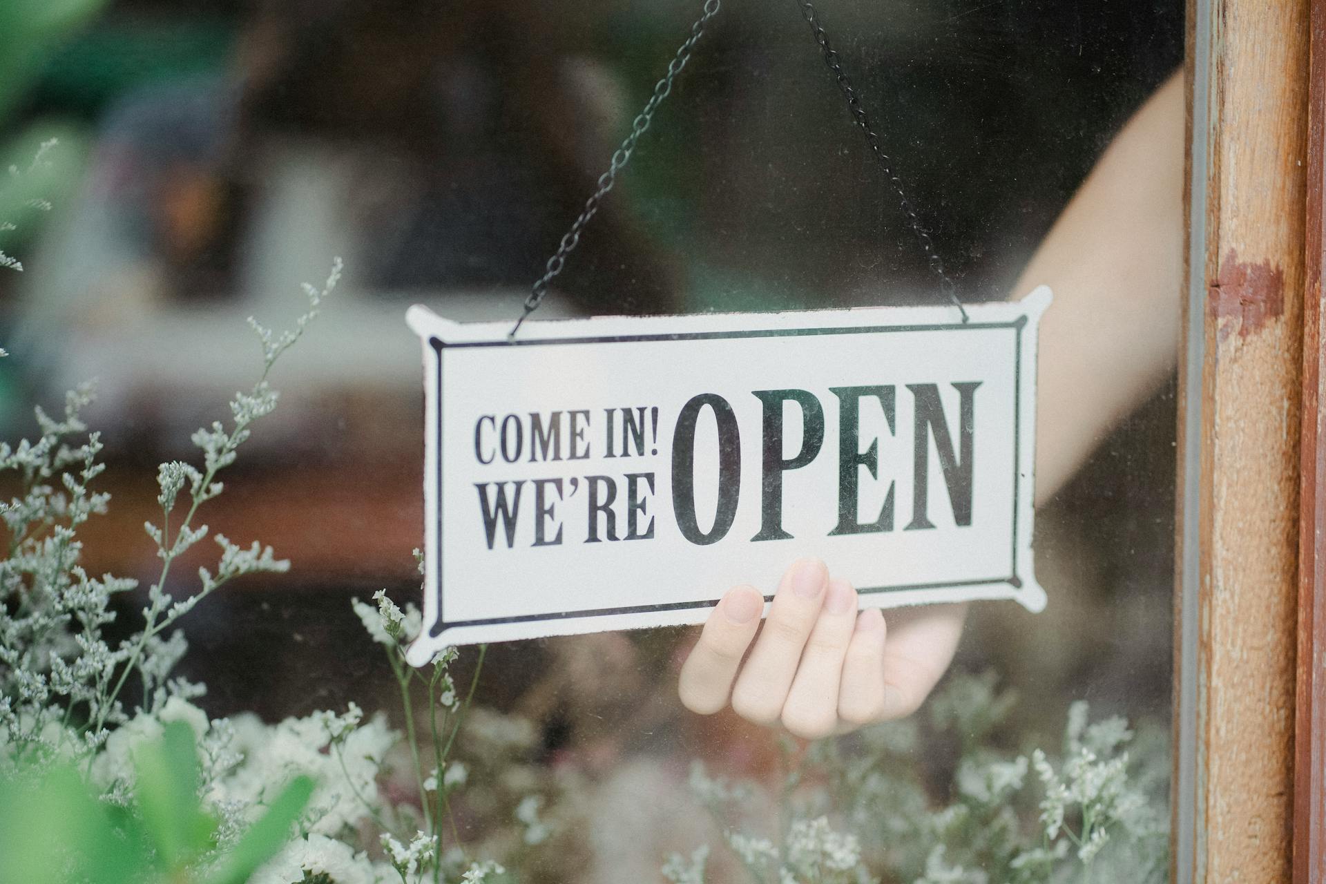 Crop anonymous person flipping signboard on window of floral shop in modern city