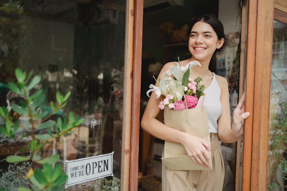 Toothy smiling female standing near flower shop and holding paper package with bouquet