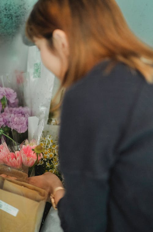 Side view of female florist choosing and taking ready made bouquet from box in floral shop