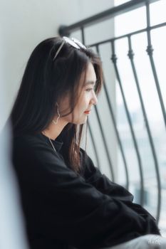 一位年轻的亚洲女子侧身坐在阳台栏杆上，面容平静，享受着片刻的宁静