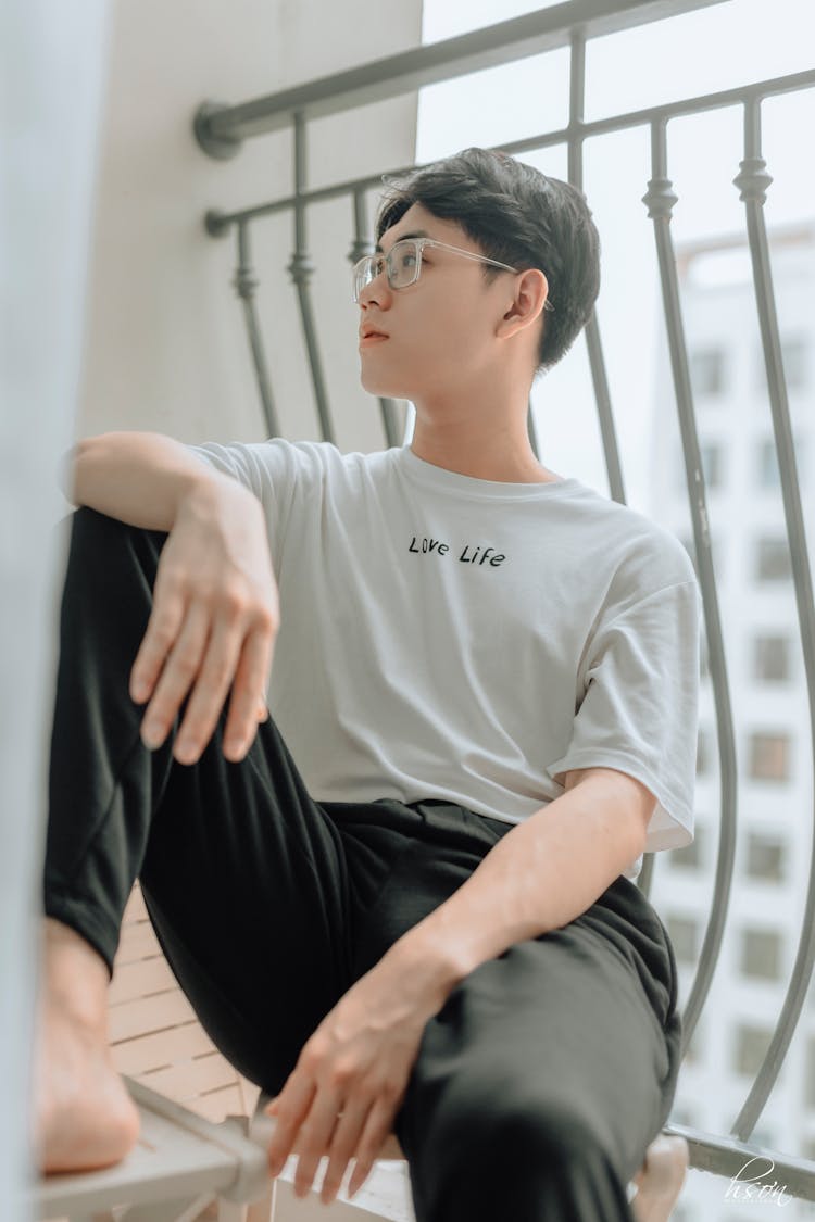 Pondering Asian Man Resting On Stool On Balcony