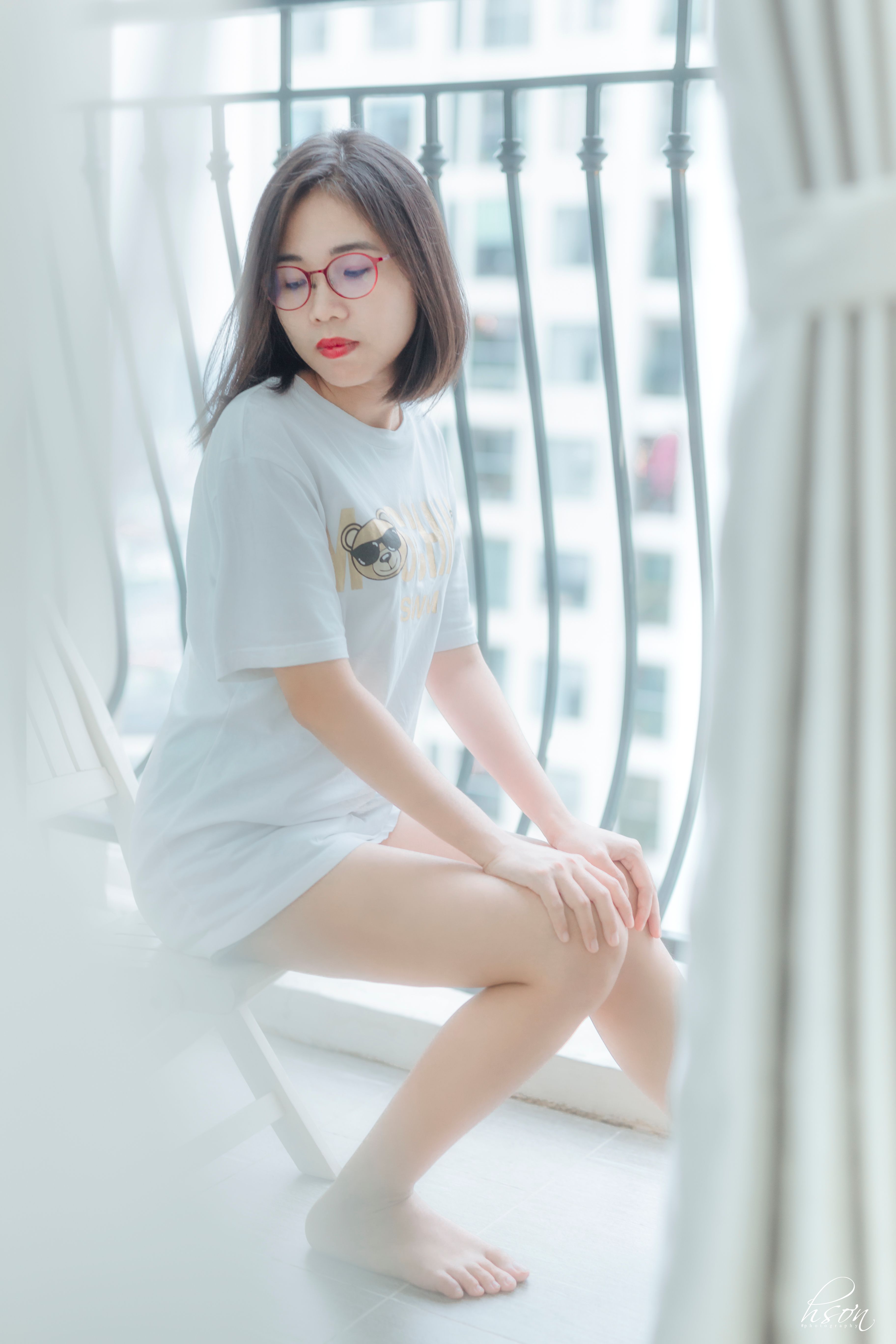 From above of young pensive barefoot ethnic lady in casual apparel and eyeglasses with makeup sitting on balcony while looking down