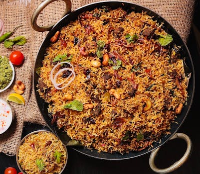 Top view of flavorful Indian biryani in a cooking pan, garnished with cashews and herbs.