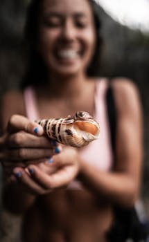 一位幸福的女子手拿螺旋桨贝壳，在海滩上享受着休闲时光