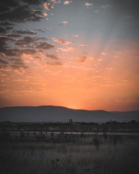 Vibrant sunset casting warm hues over a vast landscape with silhouetted mountains.