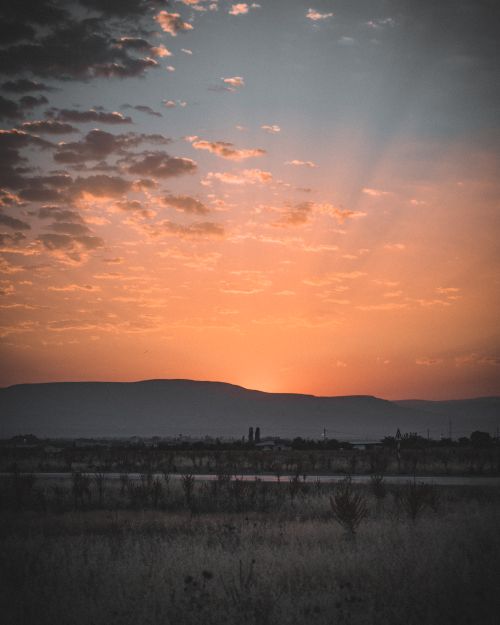 Free Vibrant sunset casting warm hues over a vast landscape with silhouetted mountains. Stock Photo