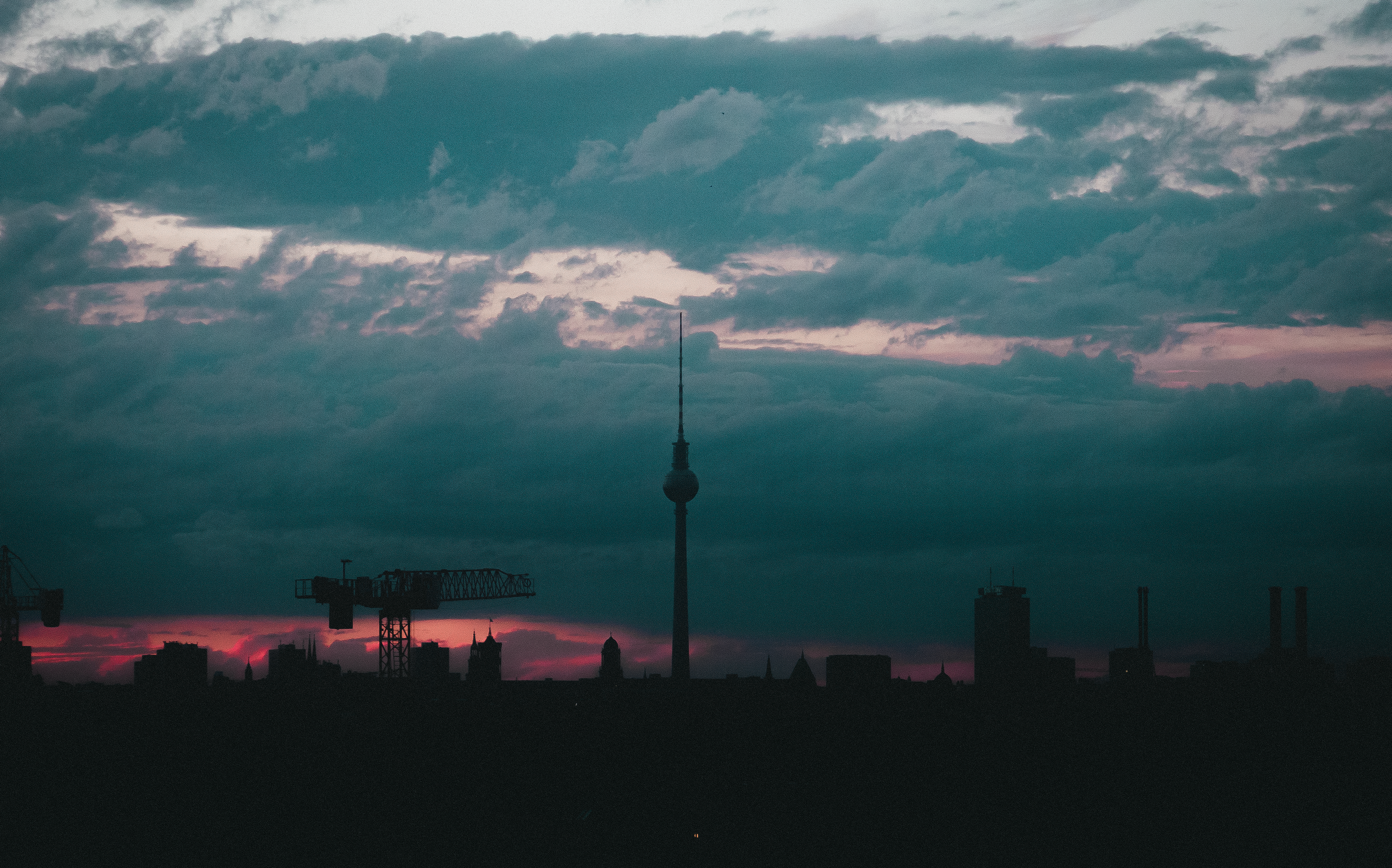 Silhouette of Berlin skyline with Fernsehturm tower at dusk, displaying dramatic clouds and vibrant colors.