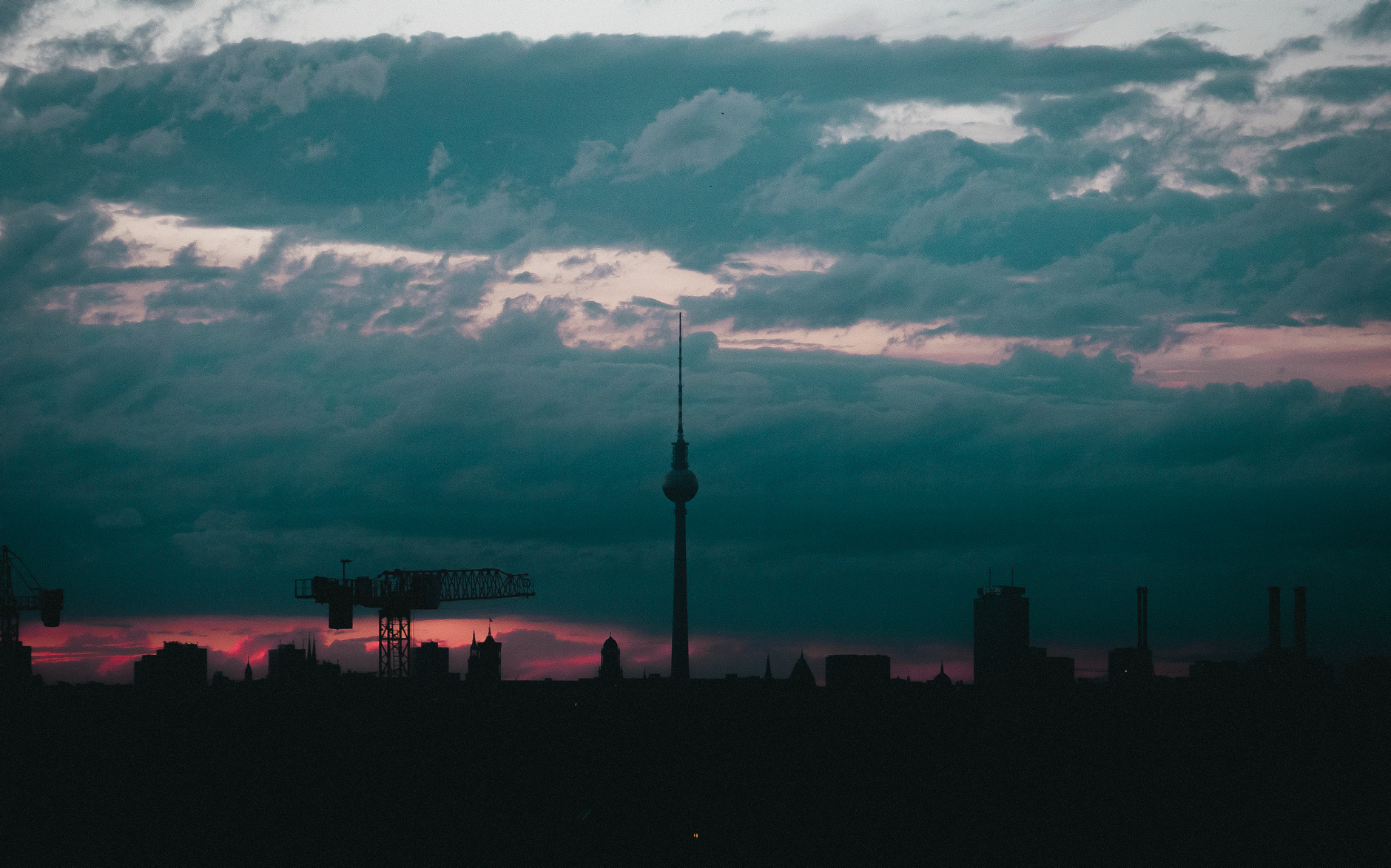 Silhouette of Berlin skyline with Fernsehturm tower at dusk, displaying dramatic clouds and vibrant colors.