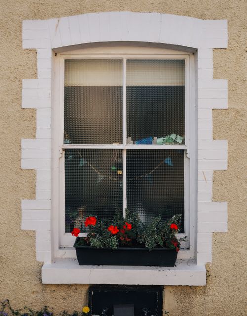 Free Close-up of a quaint window with red geraniums in a planter, adding charm to a textured yellow wall. Stock Photo