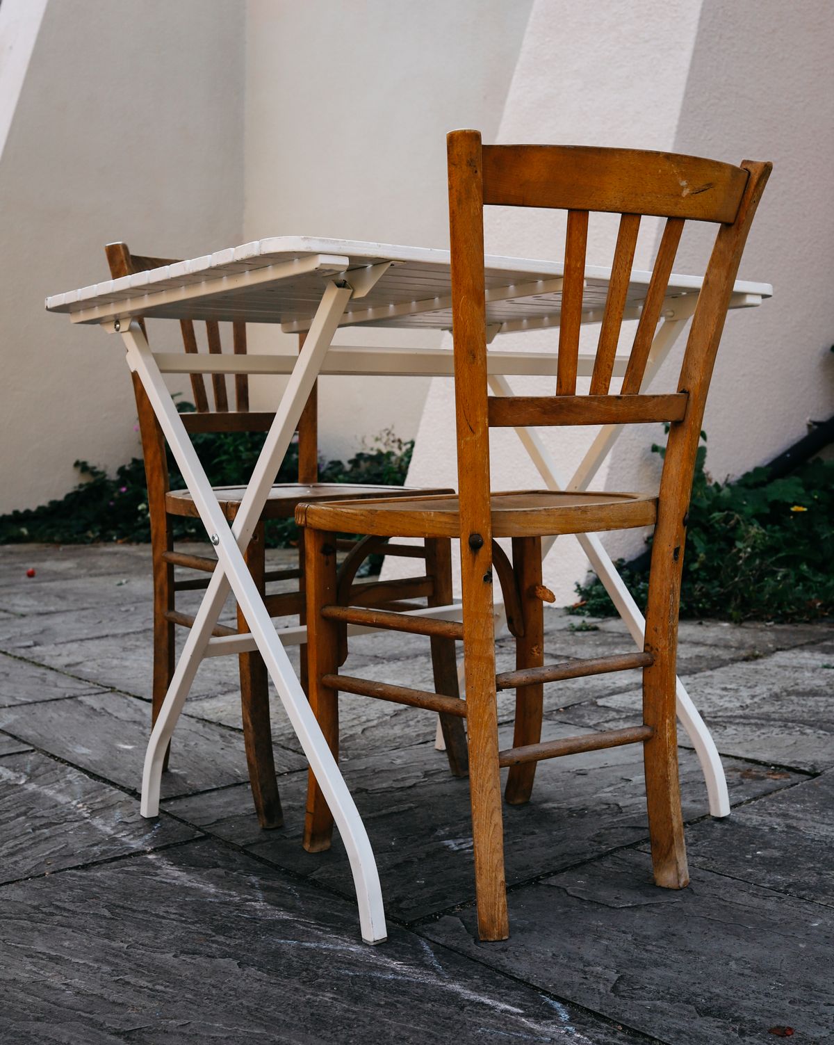 Outdoor scene with wooden chairs and a foldable table on stone pavement. Stock Photo.