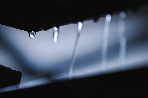 Free Closeup of water drops dripping and flowing down from dark surface in daylight Stock Photo