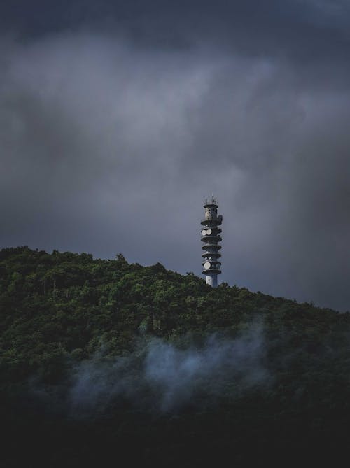 Picturesque view of modern tower in woods on hill against dark storm clouds
