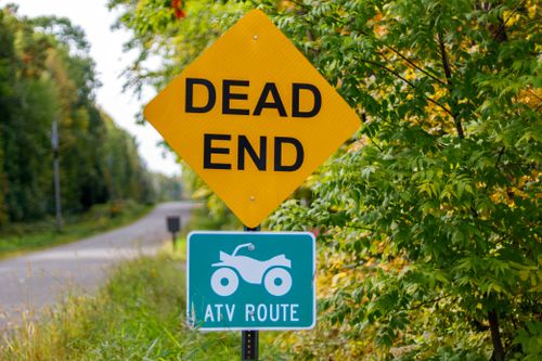 Free Yellow 'Dead End' sign with ATV route below against a lush green background. Stock Photo