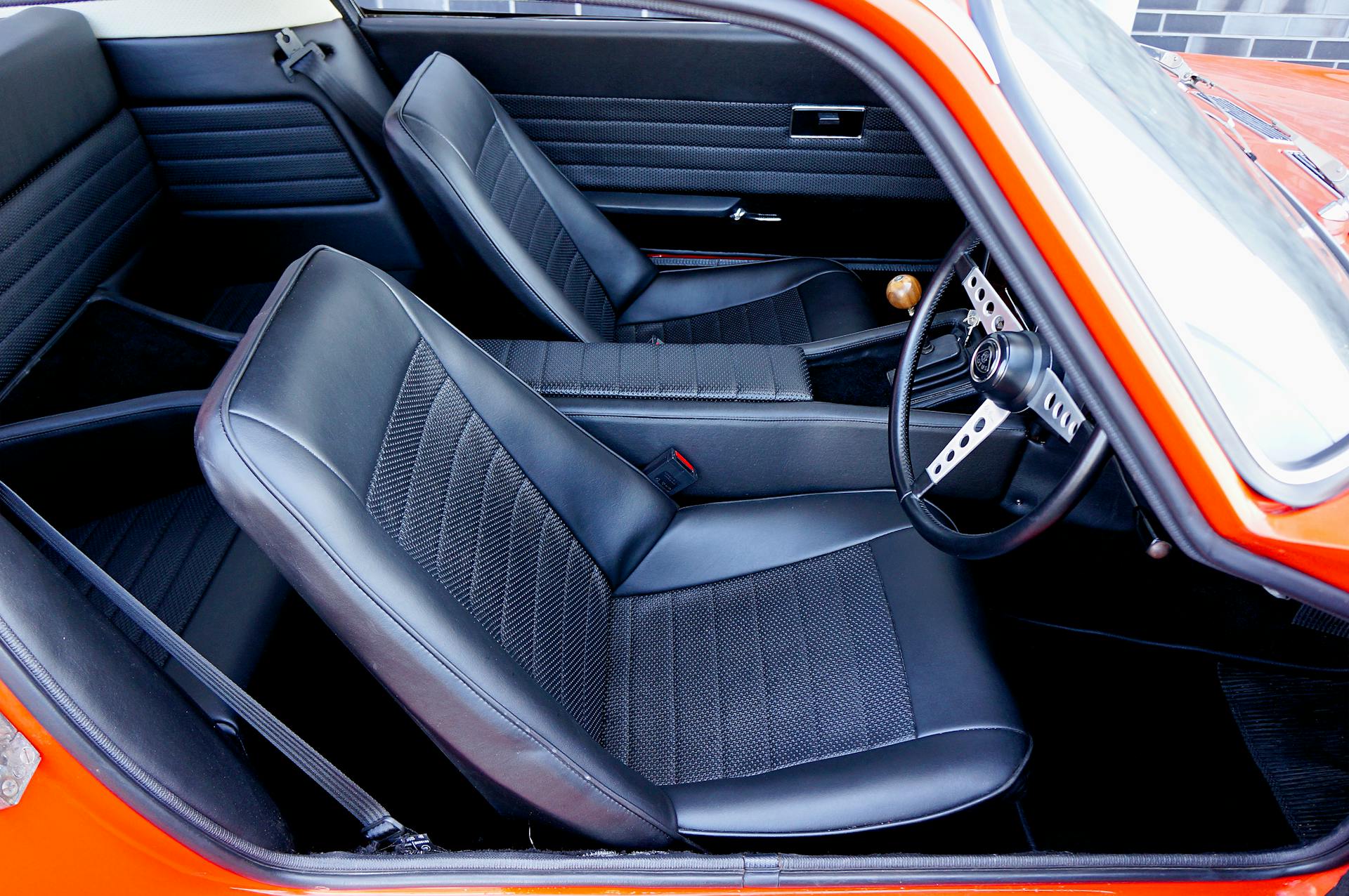 A close-up view of a classic Lotus Elan interior showcasing black leather seats and a vintage steering wheel.