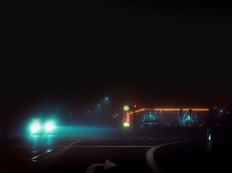 A gas station illuminated at night in Straelen, NRW, Germany with car headlights in the foreground.
