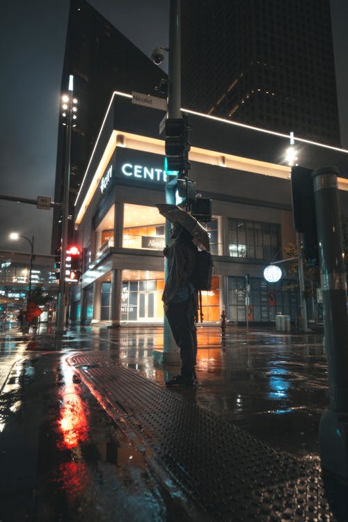 Man Holding an Umbrella Near the Street Pole