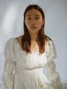 一位棕色头发、身着浪漫连衣裙的冷静年轻亚洲女士，在阳光下的白色背景前注视着镜头