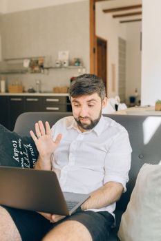 Caucasian man having a video call in a cozy home setting, sitting on a sofa with a laptop.