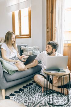 A couple comfortably working on laptops in a cozy living room setting.